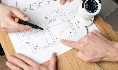 Two people discussing CCTV project. Video security equipment and blueprint on a table